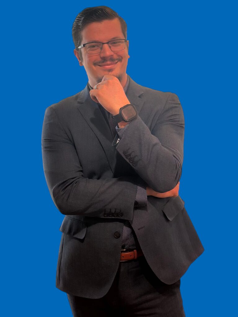 Izaak Hurst, founder of Synergy Solution IT, smiling in professional attire against a blue background, Las Vegas IT support company
